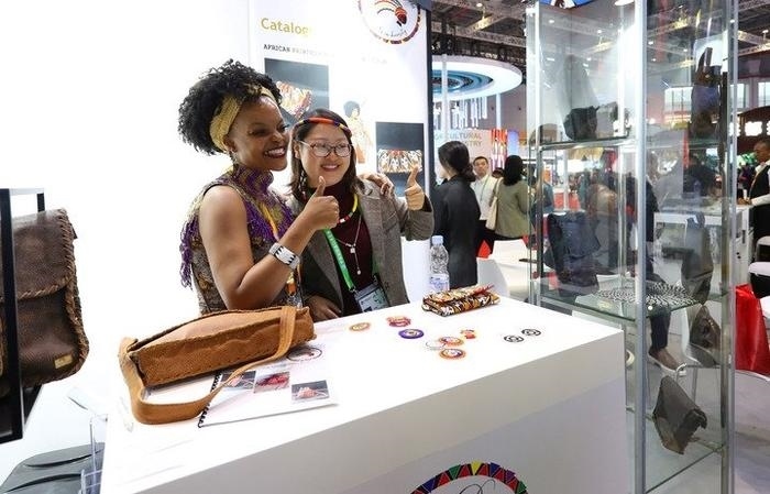 11月6日，一位參觀者（右）在第六屆進博會國家展南非展臺試戴傳統首飾。