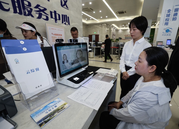 在浙江省嘉興市秀洲區(qū)王江涇鎮(zhèn)便民服務中心的“跨域通辦·云綜窗”窗口，辦理開業(yè)登記的個體工商戶（右一）通過該系統(tǒng)與江蘇省蘇州市吳江區(qū)盛澤鎮(zhèn)行政審批局工作人員視頻連線，進行身份讀取及材料線上審核（2024年5月9日攝）。新華社記者 徐昱 攝